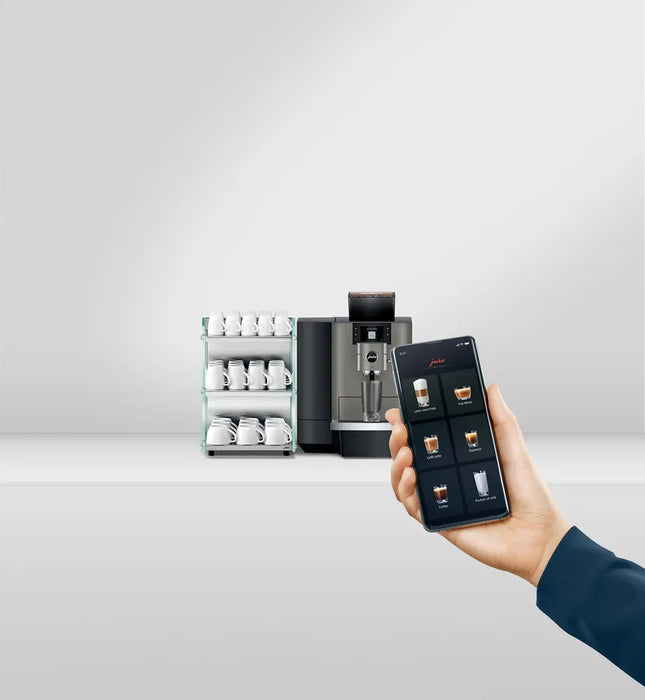JURA X10 Dark Inox zakelijke koffiemachine met smartphonebediening en kopjesrek op de achtergrond