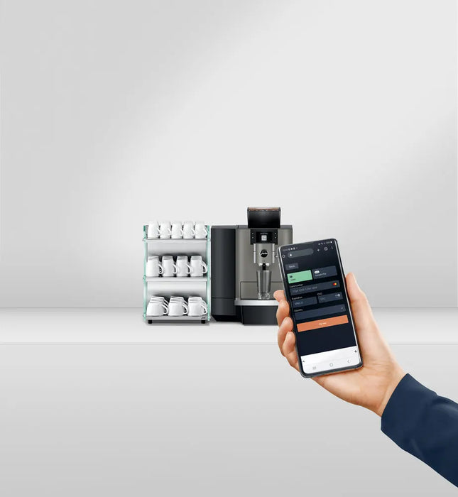 JURA X10 Dark Inox met smartphonebediening en kopjesrek op de achtergrond