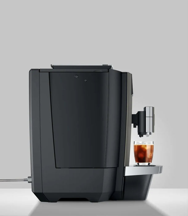 JURA X10c Dark Inox koffiemachine met zijaanzicht en glas met koude koffie op het dienblad