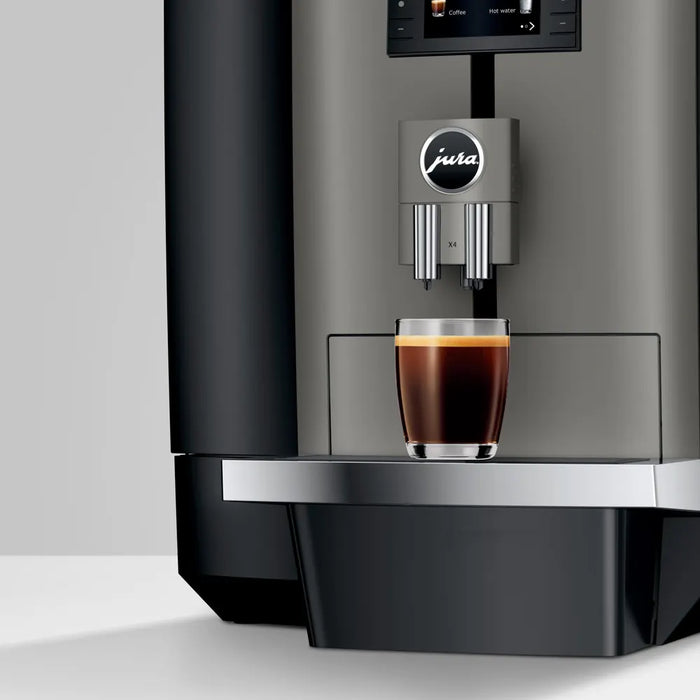 JURA X4 Dark Inox zakelijke koffiemachine met een glas versgezette koffie op het roestvrijstalen lekbakje