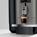 JURA X4 Dark Inox zakelijke koffiemachine met een glas versgezette koffie op het roestvrijstalen lekbakje